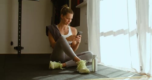 Fit Woman Using Phone in Home Gym