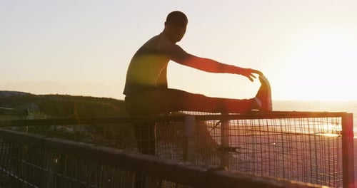 Athlete Stretching on Railing at Beach During Sunrise