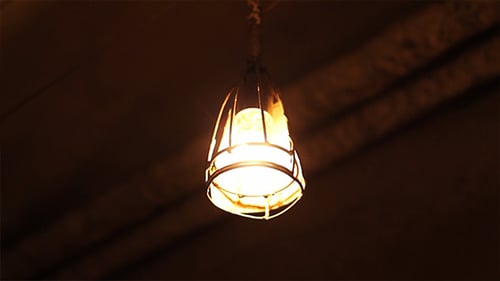 Glowing Lightbulb in Cage Flickering Warmly in the Dark
