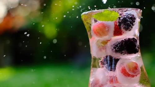 Pouring Water into Glass with Berries and Ice
