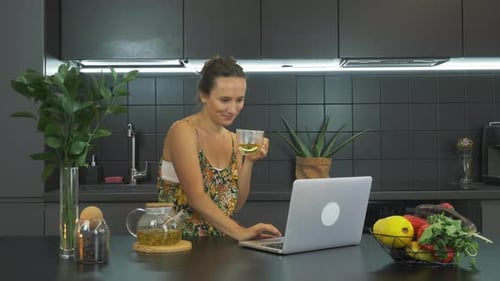 Woman Sips Tea While Working on Laptop