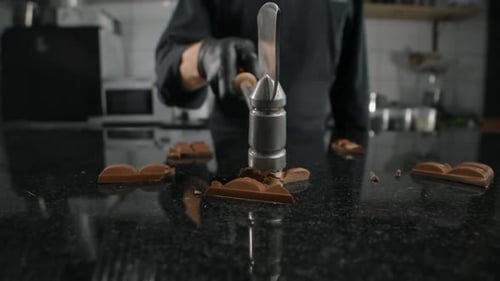 Chef Chocolatier Smashes the Milk Chocolate Bar By Kitchen Hammer on the Marble Table in Slow Motion