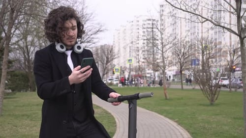 Excited Young Adult with Scooter Using Smartphone in Park