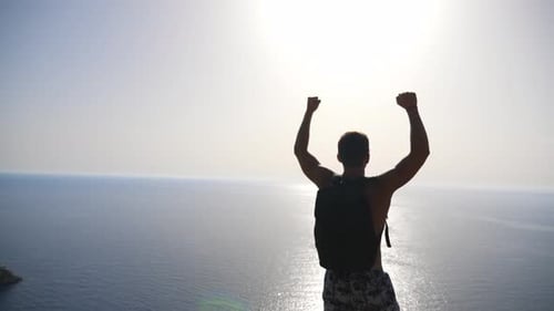 Male Hiker Standing on Edge Mountain with Raising Hands and Admiring Scenic Seascape. Man with