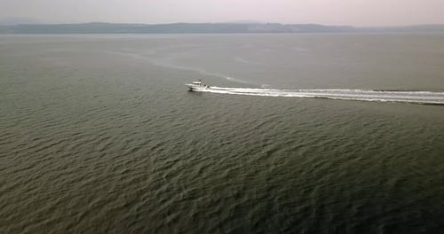 Aerial Daytime Wide Shot Flying Over Green Ocean Following A Fishing Power Boat Wake Waves With Hazy