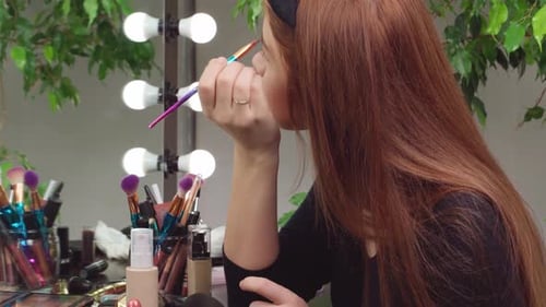 Woman Applies Makeup in Front of Mirror