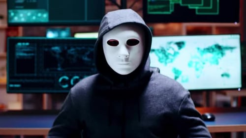 Masked Figure Sits Before Multiple Computer Screens