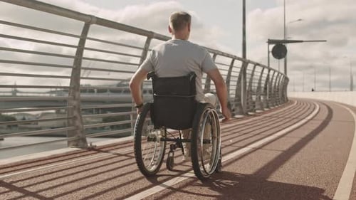 Man with Disability Riding Wheelchair along Jogging Track on Bridge