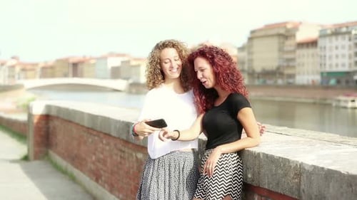 Two happy girls looking at smart phone with city on background