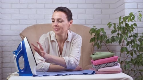 Woman sitting at table with iron and clothing