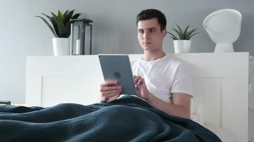 Young Adult Man Using Tablet in Bed