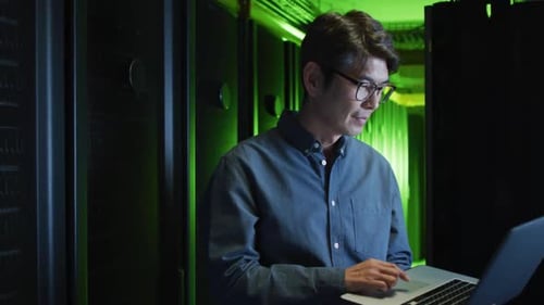 Lächelnder asiatischer männlicher IT-Techniker, der einen Laptop benutzt, um den Computerserver zu überprüfen