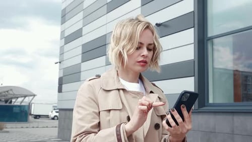 Stylish Business Woman in Jacket Walking Around the City and Text Messaging on Smartphone