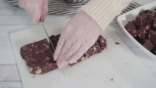 Step by step. Cutting homemade macadamia fudge on a white cutting board.