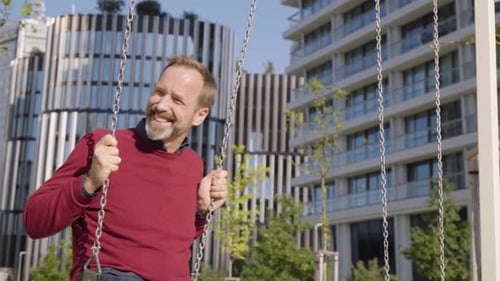 Smiling Man Having Fun on Swing in Urban Park