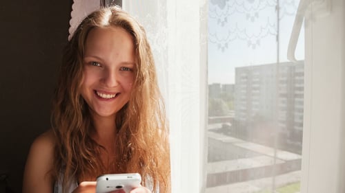 Young Woman Uses Smartphone by Window
