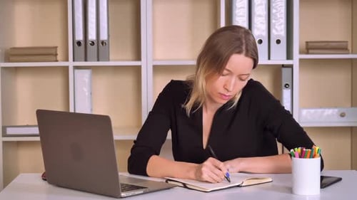 Woman Writing in Notebook at Office Desk