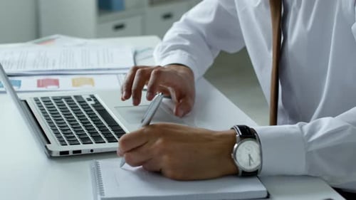 Close Up of Businessman Using Laptop and Taking Notes