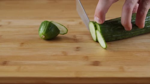 Hands Slicing A Green Cucumber On The Chopping Board With A Knife - close up