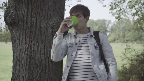 Young Adult Drinking Coffee Leaning Against Tree