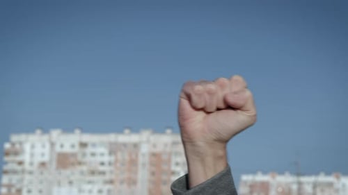 Hand With Fist Raised In Front Of Building