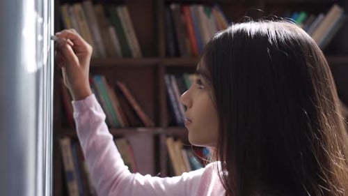 Serious Indian Latin Kid School Girl Pupil Holding Chalk Writing on Blackboard
