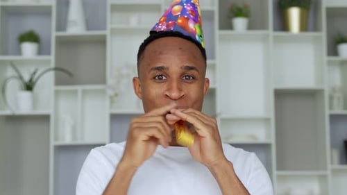 African Man Having Fun at a Party Wearing a Holiday Hat While Blowing a Party Horn.