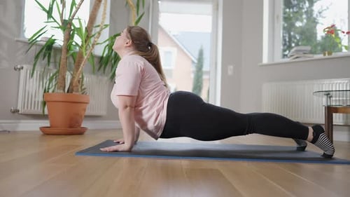 Vista lateral de uma mulher caucasiana flexível de tamanho grande em pose de cobra no tapete de exercícios