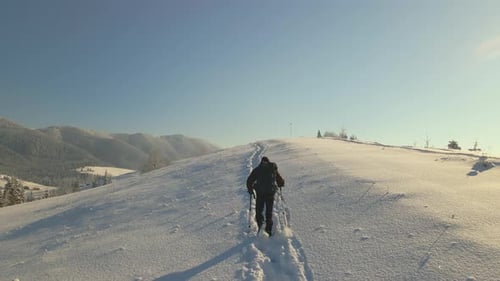 Hiker with Backpack Walking on Snowy Mountain Hillside on Cold Winter Day