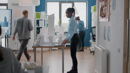 Woman Engineer Working with Laptop and Building Model to Design Blueprints on Paper