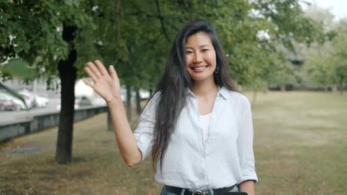Zeitlupenporträt eines asiatischen Mädchens, das im Freien im Stadtpark mit der Hand winkt