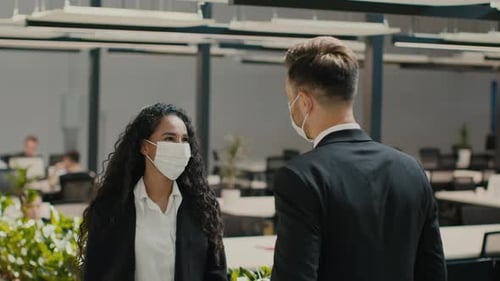 Businessman And Businesswoman Wearing Masks Bumping Elbows Talking In Office