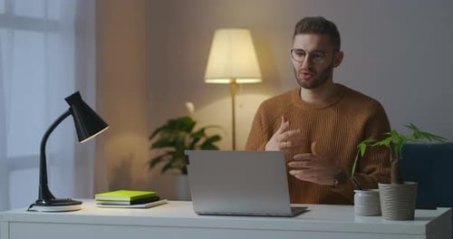 Jovem vestido com suéter marrom está dando as boas-vindas aos interlocutores na conferência on-line de bate-papo por vídeo de trabalho