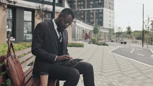 Man in Suit Using Tablet on Bench in City