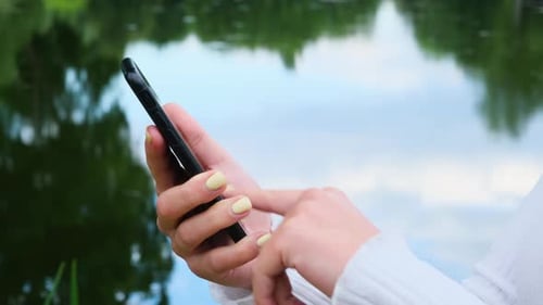 Close Up Woman Hands Uses the Phone on the Background of the Park.