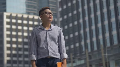 Portrait handsome Asian businessman holding a book standing looking around the urban city.