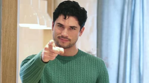 Man Points at the Camera, Smiling Indoors