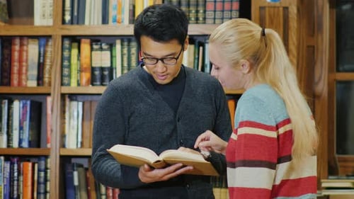 Asian Man with Glasses and Caucasian Women Standing Together Watching the Book in the Library.