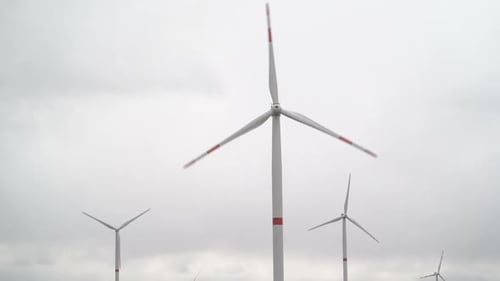 Motion the Blades of a Large Wind Turbine in a Field Against a Background of Cloudy Grey Sky on the