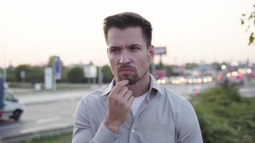 A Young Caucasian Man Thinks About Something in an Urban Area Busy Intersection in the Background