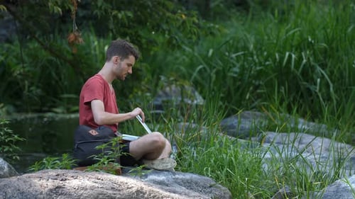 Young adult uses laptop outdoors in nature