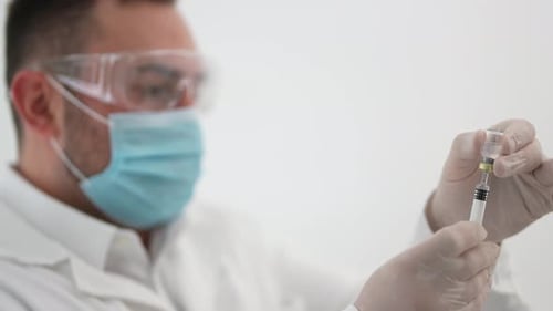 Man Extracts Fluid From Vial with Syringe