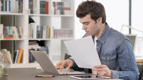 Man Using Laptop with Documents in Office