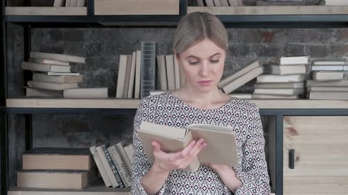 Young woman chooses a book in the library, She is in corridor between the books
