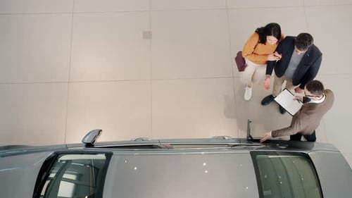 Top View of Young Couple Purchasing Automobile in Car Dealership Talking To Sales Manager