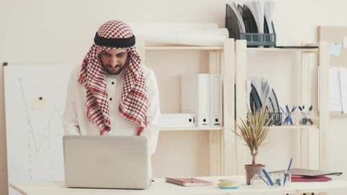 The Sheikh Is Working on a Laptop, Looking at the Camera and Smiling. An Arab Businessman in Kandur