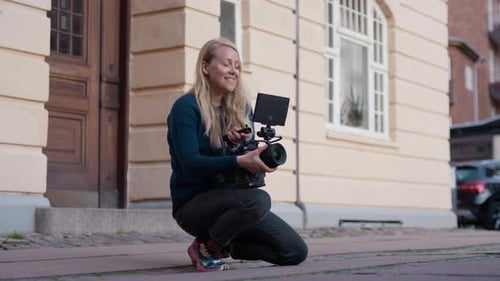 Woman Operating Professional Camera Kneeling in Urban Setting