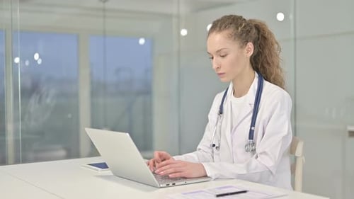 Cheerful Young Female Doctor Working on Laptop in Office