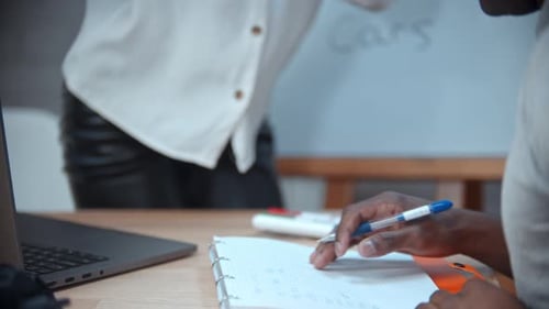 Une femme blanche et un homme noir ayant une leçon d'anglais - une femme se penchant vers le carnet et