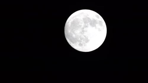 Enorme luna llena resplandeciente vista desde la Tierra a través de las nubes contra el cielo nocturno estrellado